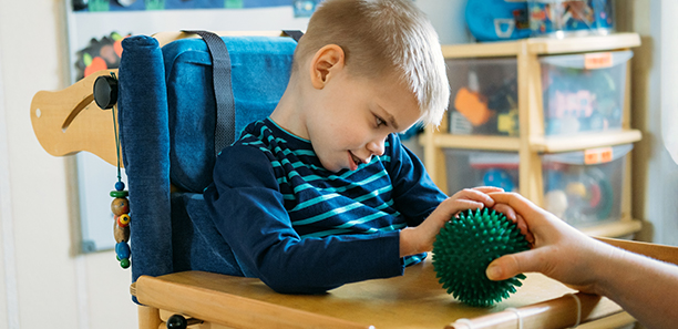 Sensory Activities for kids with disabilities. Preschool Activities for Children with Special Needs. Boy with with Cerebral Palsy in special chair play with mom at home