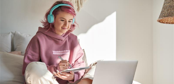 Girl sitting on bed wearing headphones with laptop.png